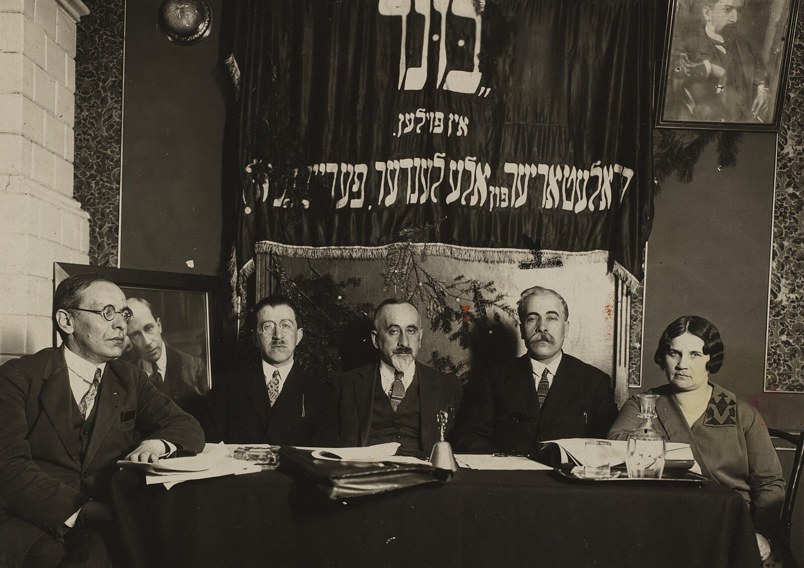 A sepia photo of 4 men and 1 woman sitting at a table, facing the camera