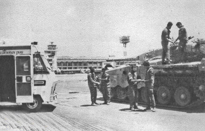 Black and white photo of Israeli tank with six soldiers, two standing on the tank, and a civilian vehicle nearby