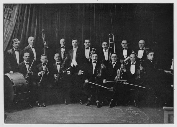 A black and white photo of 15 men in tuxedos holding various instruments and looking at the camera